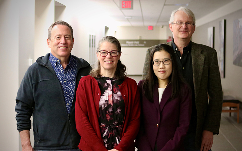 Four people standing in a hallway smile for the camera.