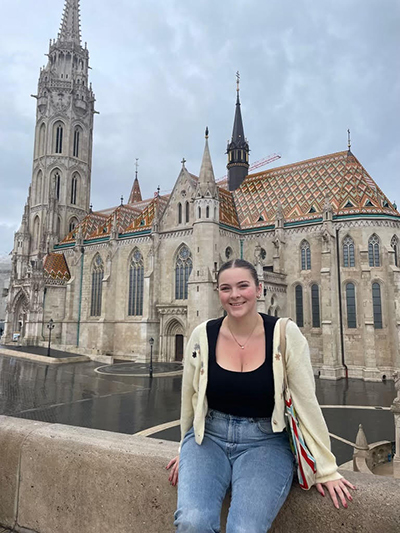 Schar School junior Maggie Reier sitting and smiling in front of a building in Budapest