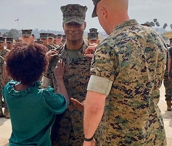 A woman with her back to the camera pins a medal to a man in a military uniform who is smiling.